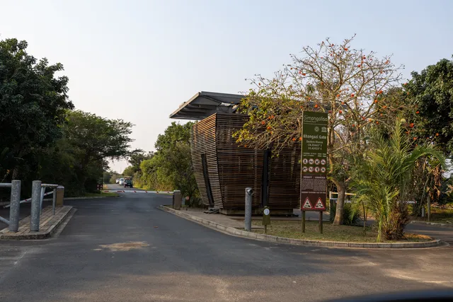 The timber-clad entrance gate to the reserve, with the park road, information signage and flowering coral trees alongside.